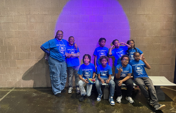  8 students and 1 teacher smiling to take a picture against a wall with a purple circle 